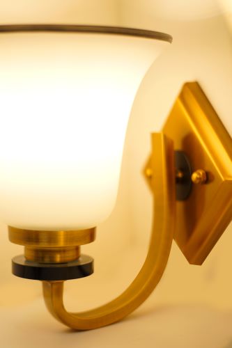 A close-up of a metal wall sconce with a frosted glass shade mounted on a golden diamond-shaped base.