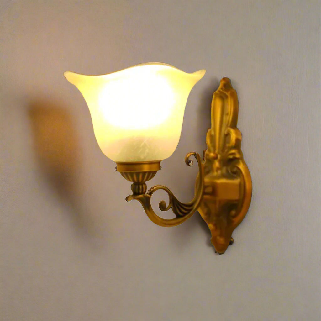 A vintage-style metal wall lamp with a frosted glass shade, equipped with a led lamp E27 illuminating a warm yellow light against a light grey wall.