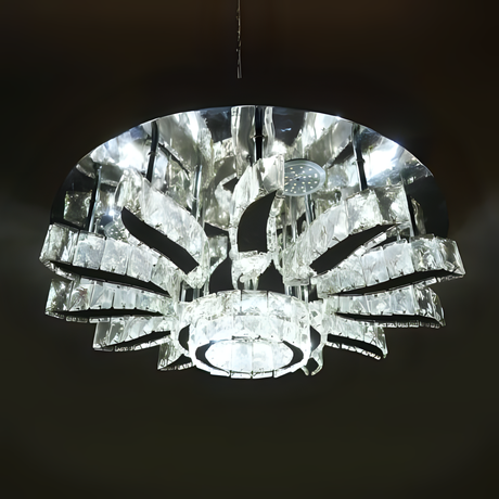 A grand round chandelier with multiple outward-bending arms made of clear crystal, forming a radial pattern and suspended from a dark ceiling; it gives off cool white lighting and adds dramatic flair to large spaces.

