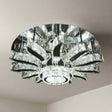 A grand round chandelier with multiple outward-bending arms made of clear crystal, forming a radial pattern and suspended from a dark ceiling; it gives off cool white lighting and adds dramatic flair to large spaces.
