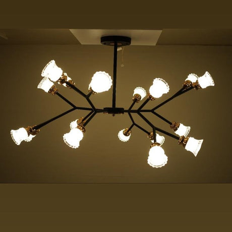 A modern ceiling chandelier with a flower design, black metal frame, and several white globe-shaped light covers arranged on branching arms, mounted on a beige ceiling.