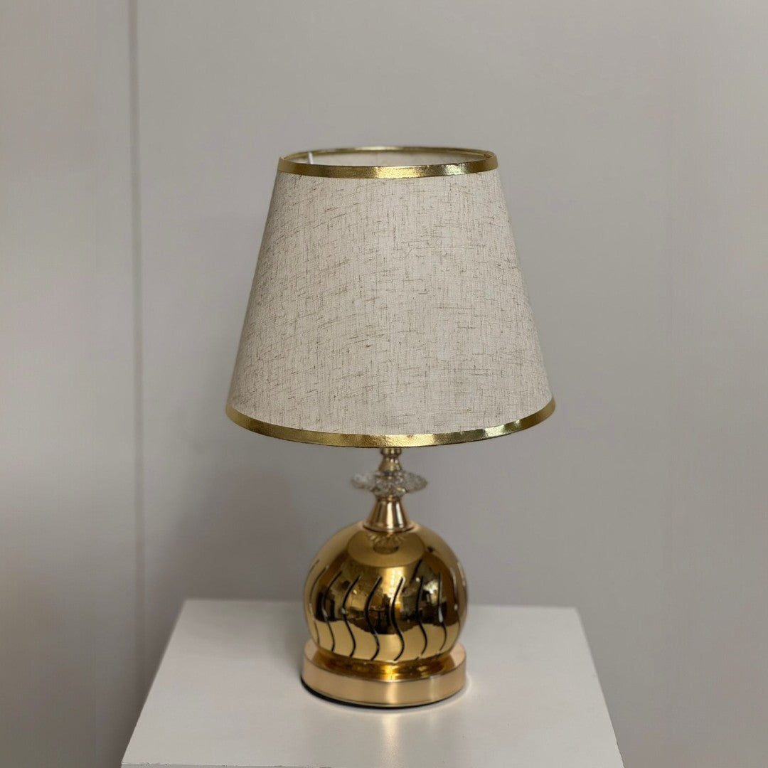 Elegant gold and beige table lamp with a spherical textured gold base and a beige-colored fabric shade.
