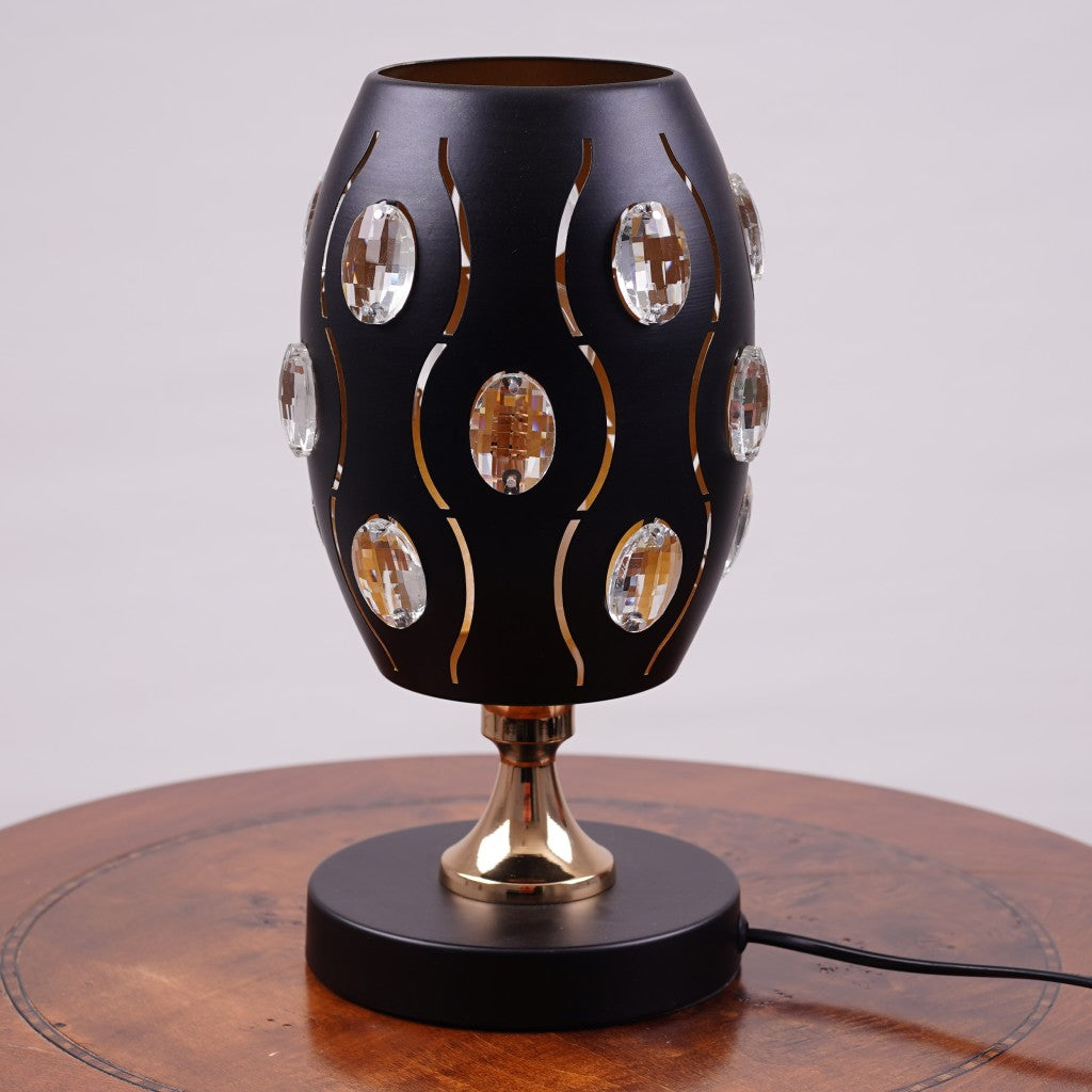 A black globe table lamp with a geometric design, adorned with crystal beads, gold accents, and a sleek base, sit on a wooden table. It features an LED light with an E27 bulb, casting a warm, stylish glow.
