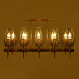 A gold-finished linear chandelier with exposed bulbs, casting a warm glow in a dimly lit setting.