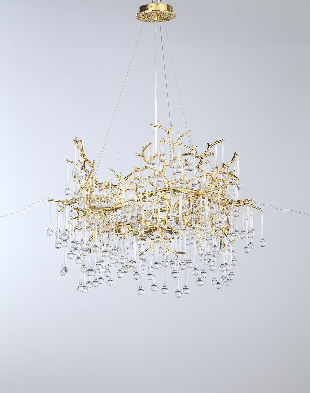 A suspended gold chandelier with a cascading design featuring delicate branches and crystal droplets.