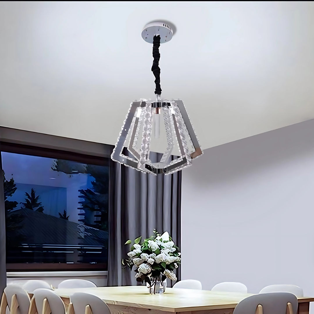 A contemporary geometric crystal pendant chandelier with a polygonal layered design, featuring clear glass panels and a mirrored frame, casts elegant light over a sophisticated dining room. Below, a sleek dining table is paired with white chairs, and a decorative vase serves as the centerpiece.
