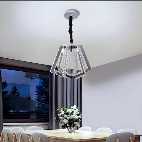 A contemporary geometric crystal pendant chandelier with a polygonal layered design, featuring clear glass panels and a mirrored frame, casts elegant light over a sophisticated dining room. Below, a sleek dining table is paired with white chairs, and a decorative vase serves as the centerpiece.