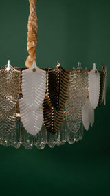 A side angle of the chandelier, showing its symmetrical arrangement of glass leaves, suspended by a twisted golden chain for an elegant look.