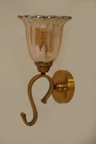 A metal wall sconce with a curved arm and a transparent fluted glass shade, blending modern and traditional elements.