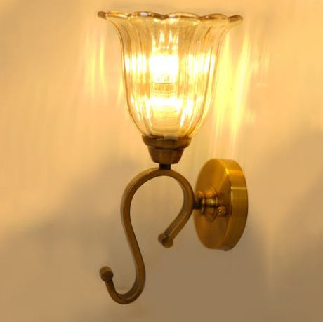 A gold and curved-arm wall sconce with a ribbed glass shade, equipped with an a led lamp E27 casting a warm glow.