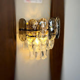 A decorative gold wall light featuring grey circular elements with cascading crystal droplets, reflecting warm light beautifully.
