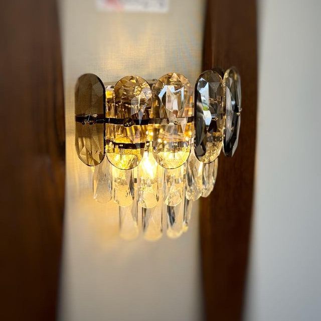 A decorative gold wall light featuring grey circular elements with cascading crystal droplets, reflecting warm light beautifully.