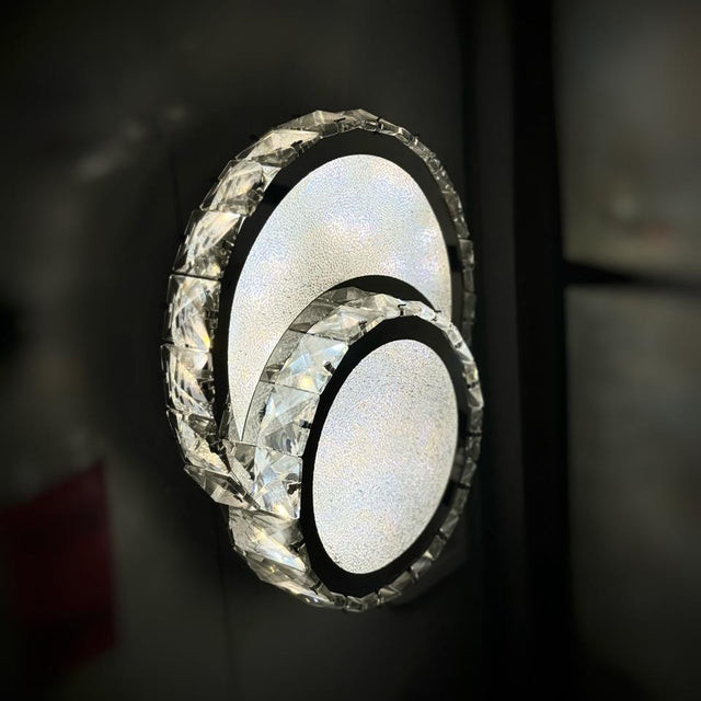  A set of three overlapping circular LED wall lights with crystal detailing, mounted on a dark wall.