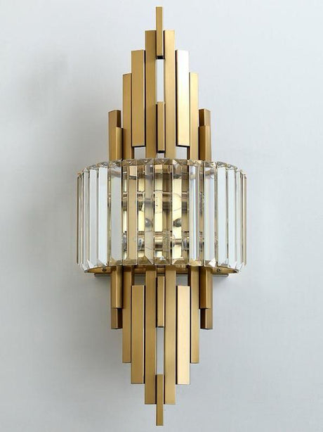 A modern gold and crystal wall sconce with vertical rods and glass elements, fixed on white wall.