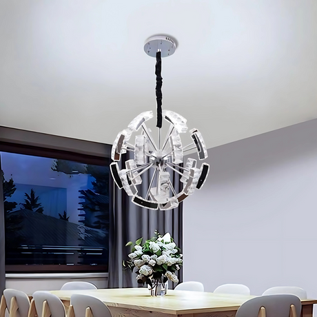A contemporary circular crystal pendant chandelier with a layered design, featuring clear glass panels and a mirrored frame, hangs from a light-colored ceiling and casts elegant light over a sophisticated dining room. Below, a sleek dining table is paired with white chairs, and a decorative vase serves as the centerpiece.