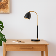 Modern desk with a black and gold lamp, notebook, and pen on a light wooden surface.