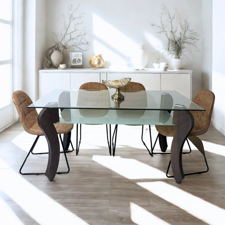  A modern dining set with a glass tabletop and sculptural black legs, bathed in natural light and surrounded by six brown cushioned chairs.