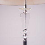 Tall modern floor lamp with a sleek glass and chrome base, placed in a minimalistic setting.