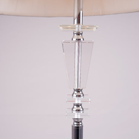Tall modern floor lamp with a sleek glass and chrome base, placed in a minimalistic setting.