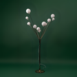 A modern artistic floor lamp with multiple spherical white bulbs branching out from a central metallic stand, set against a green background.