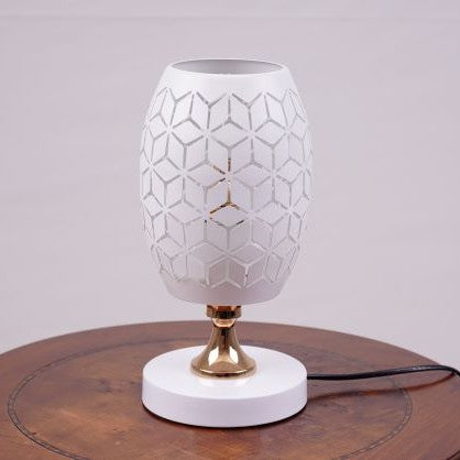 A white modern table lamp with a geometric design, gold accents, and a sleek base sits on a wooden table. It features an LED light with an E27 bulb, casting a warm, stylish glow.