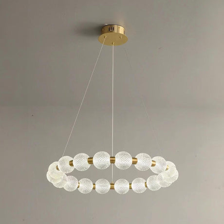 A contemporary circular chandelier with frosted spherical glass shades arranged in a ring, suspended by thin wires from a gold ceiling mount.