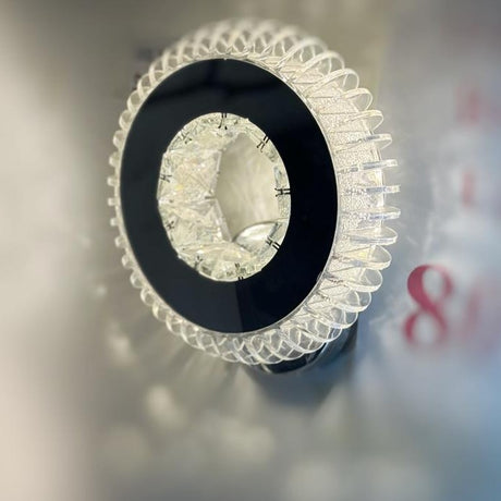 A round crystal wall sconce with a layered circular pattern, giving off a radiant effect.