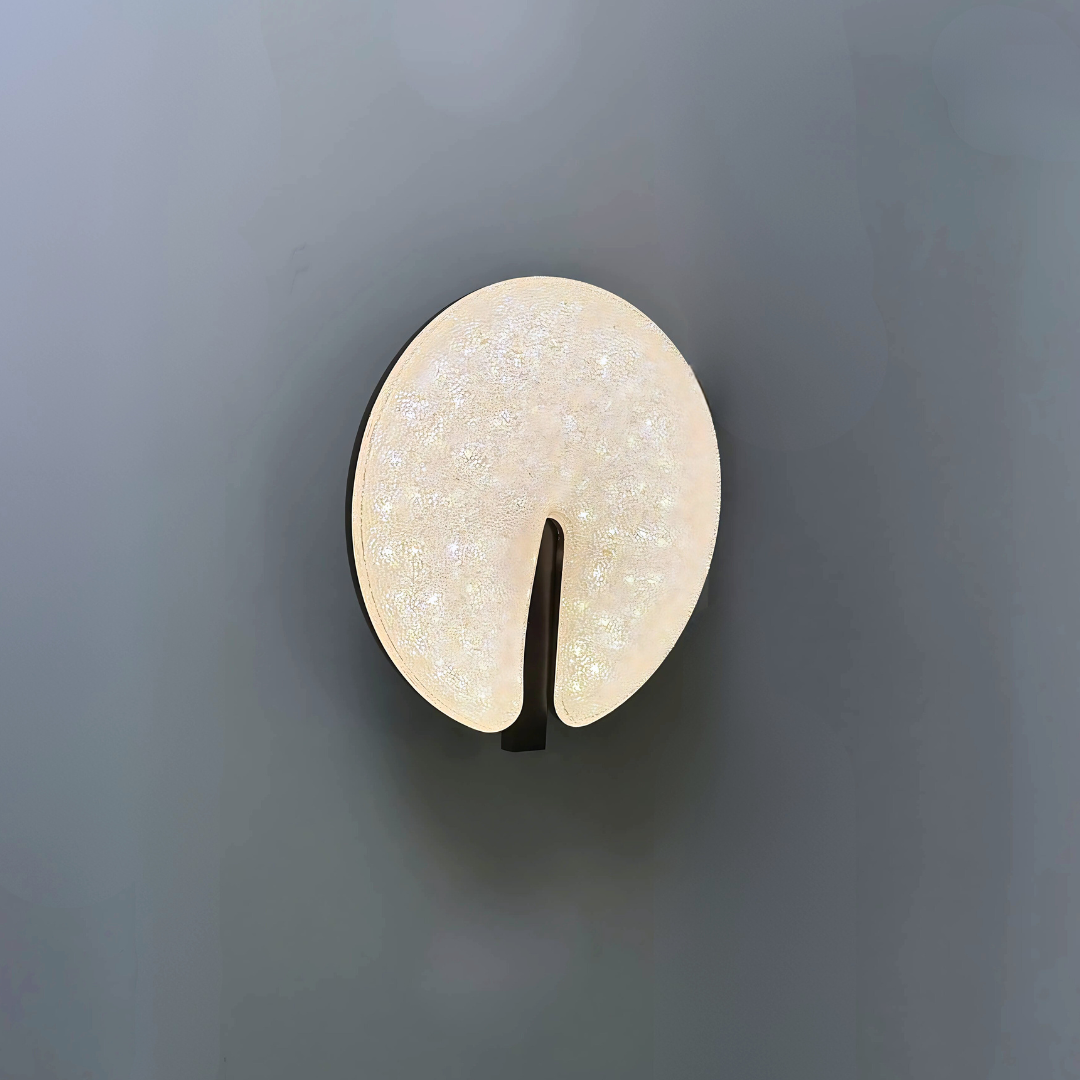 Modern circular LED wall light fixture with a sparkling textured surface and a sleek brown cut-out design, mounted on a dark-colored wall.
