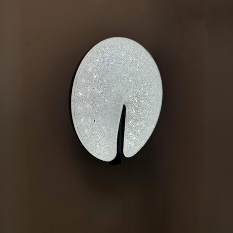 Modern circular LED wall light fixture with a sparkling textured surface and a sleek brown cut-out design, mounted on a dark-colored wall.
