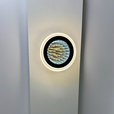 Modern circular LED wall light with a futuristic infinity mirror effect, emitting warm and cool light patterns inside a glossy black and white frame.