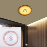 A circular flush ceiling light with a soft golden border and a small central floral detail, installed on a beige ceiling near wood paneling; it emits a cozy, warm yellow light and is about 40 cm in diameter.