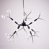 A modern, black branching chandelier with multiple exposed bulbs housed in clear, globe-shaped glass covers, resembling a molecular structure, hanging against a pale background.