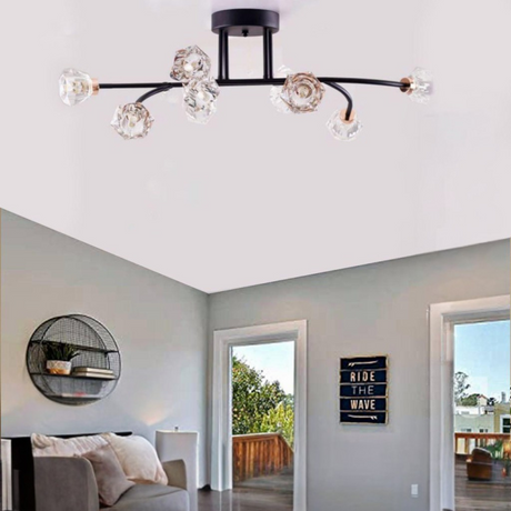 A black and gold ceiling-mounted light fixture with multiple curved arms and crystal-like bulbs, installed on a white ceiling in a stylish living room featuring minimalist decor, a round wall shelf, a cozy sofa, and a decorative sign that reads 'Ride The Wave