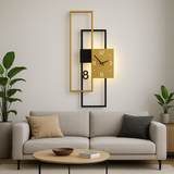 Modern rectangular wall clock in black and gold metal with warm LED backlight, mounted above a beige sofa in a minimalist living room. The clock features geometric frames and a square face with white numerals, adding a sleek contemporary touch to the interior décor.
