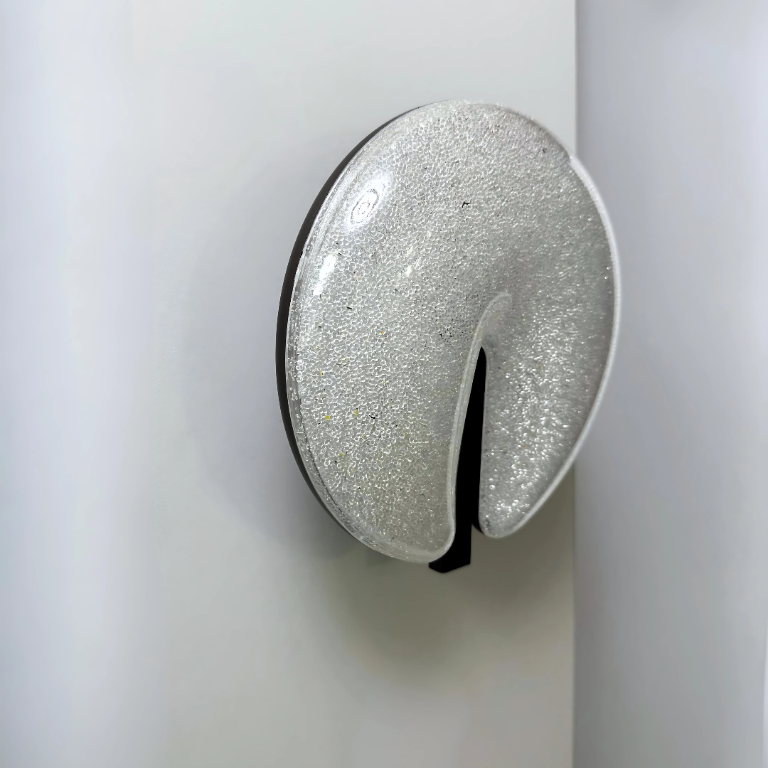 Modern circular LED wall light fixture with a sparkling textured surface and a sleek brown cut-out design, mounted on a dark-colored wall.
