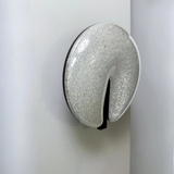 Modern circular LED wall light fixture with a sparkling textured surface and a sleek brown cut-out design, mounted on a dark-colored wall.
