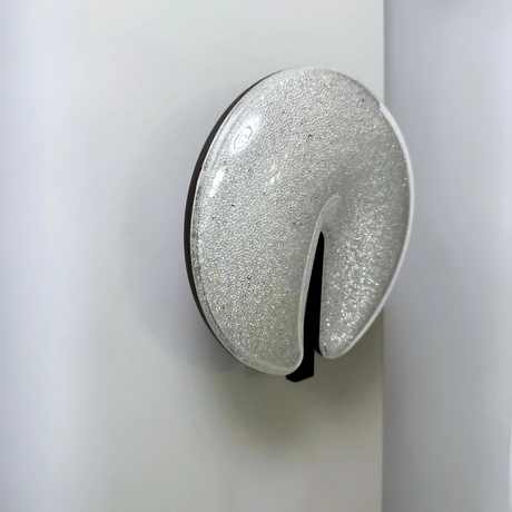 Modern circular LED wall light fixture with a sparkling textured surface and a sleek brown cut-out design, mounted on a dark-colored wall.
