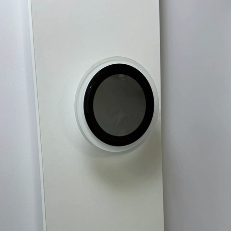 Unlit circular wall-mounted LED light with a sleek black center and white rim, blending into a minimalist white wall background.
