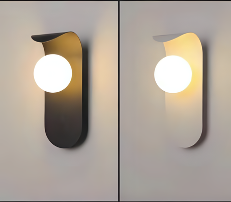 A black and white vertical wall sconce with a uniquely curved shape, featuring a spherical white glass bulb positioned at the center.
