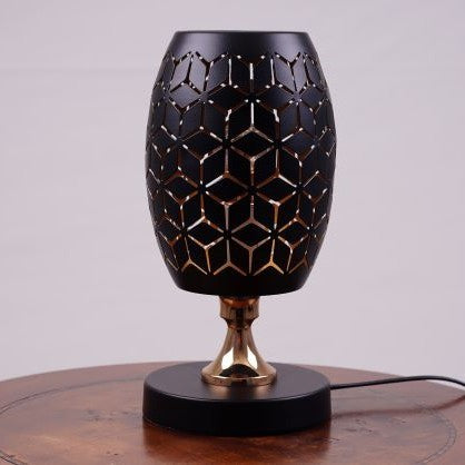 A black table lamp with a geometric design, gold accents, and a sleek base sits on a wooden table. It features an LED light with an E27 bulb, casting a warm, stylish glow.