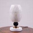 A white globe table lamp with a geometric design, gold accents, and a sleek base sits on a wooden table. It features an LED light with an E27 bulb, casting a warm, stylish glow.