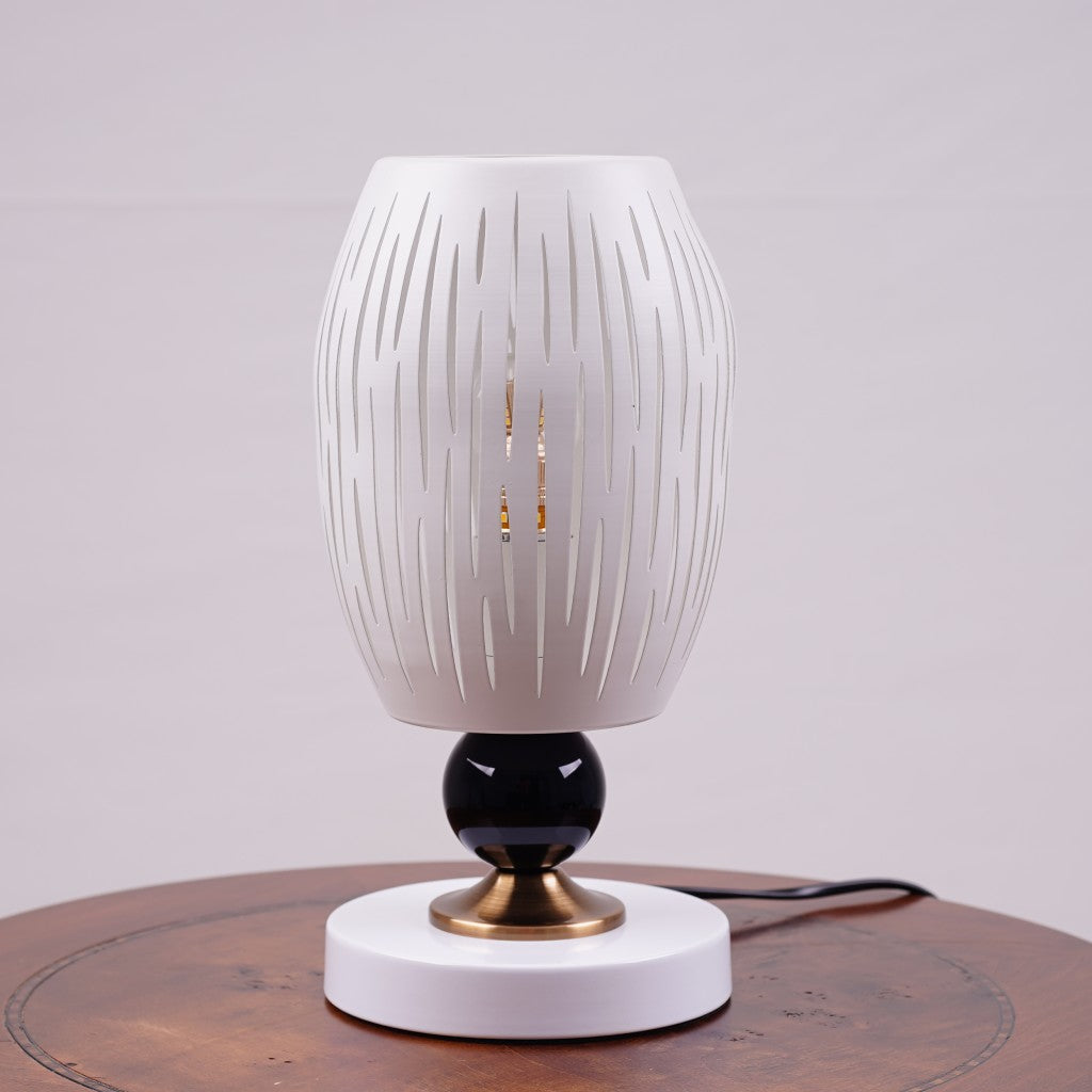 A white globe table lamp with a geometric design, gold accents, and a sleek base sits on a wooden table. It features an LED light with an E27 bulb, casting a warm, stylish glow.