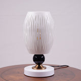 A white globe table lamp with a geometric design, gold accents, and a sleek base sits on a wooden table. It features an LED light with an E27 bulb, casting a warm, stylish glow.