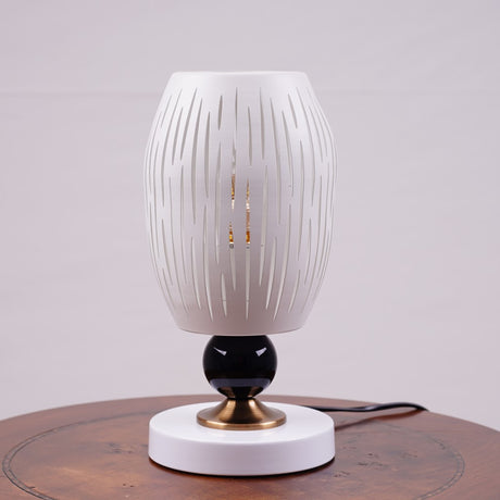 A white globe table lamp with a geometric design, gold accents, and a sleek base sits on a wooden table. It features an LED light with an E27 bulb, casting a warm, stylish glow.