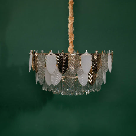 A full view of the chandelier against a green background, highlighting its circular frame adorned with alternating gold, white, and clear glass leaves.