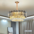 A modern chandelier with gold  accents hanging in a well-lit living room with neutral-colored curtains.