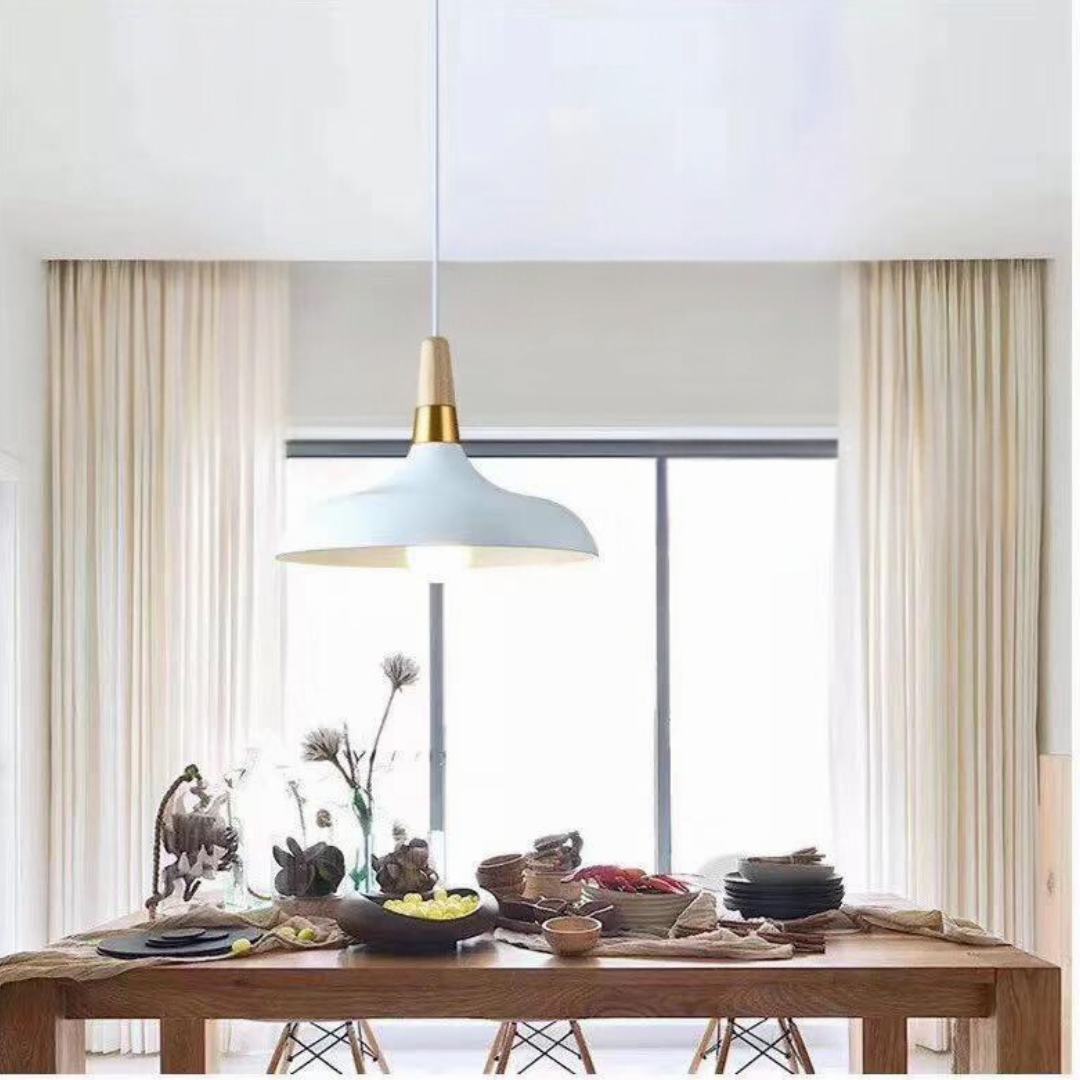A sleek white and gold pendant light with a smooth, curved shade, illuminating a wooden dining table.
