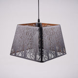 A black square-shaped pendant lampshade with intricate tree patterns cut into the metal frame.

