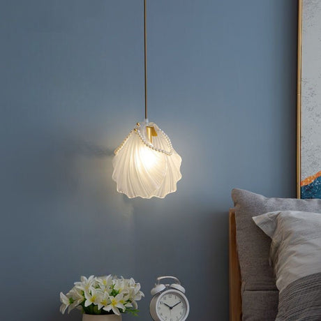 A delicate white shell-shaped pendant light hanging beside a bed, casting a soft glow against a blue wall.