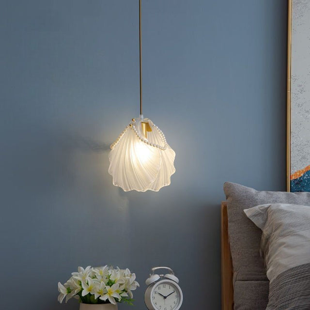 A delicate white shell-shaped pendant light hanging beside a bed, casting a soft glow against a blue wall.